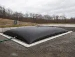 IEC Dewatering Tube installed on a lined gravel pad for sludge dewatering and filtrate control at a wastewater site.